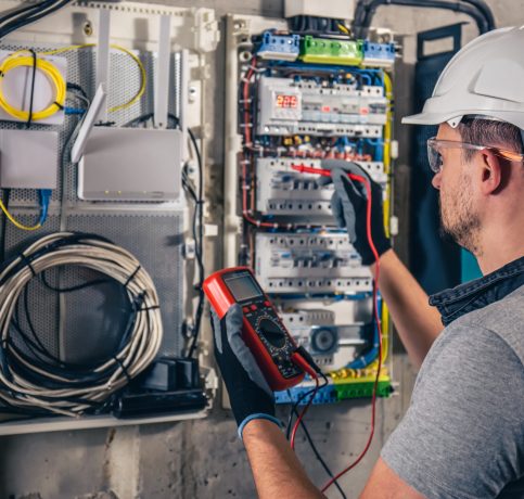 Man, an electrical technician working in a switchboard with fuses. Installation and connection of electrical equipment. Professional uses a tablet.