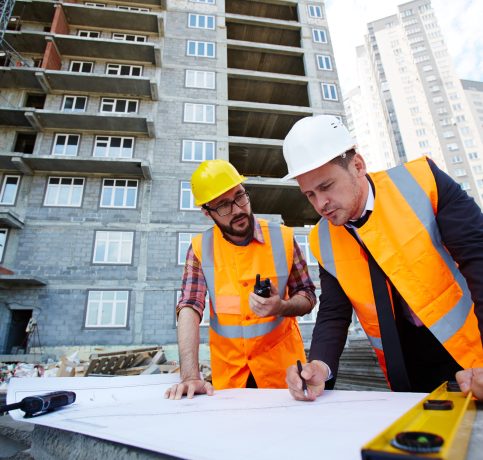 Modern engineer pointing at sketch in blueprint while explaining it to colleague